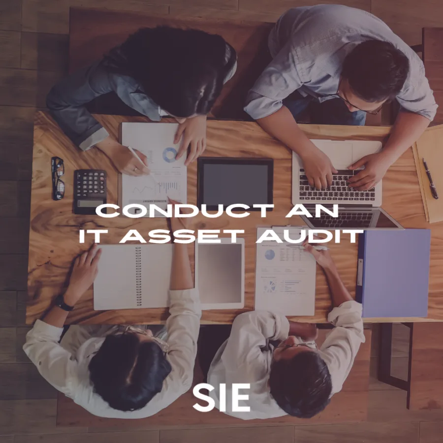 IT professionals conducting an IT asset audit around a conference table, reviewing hardware and documentation for end-of-life planning.